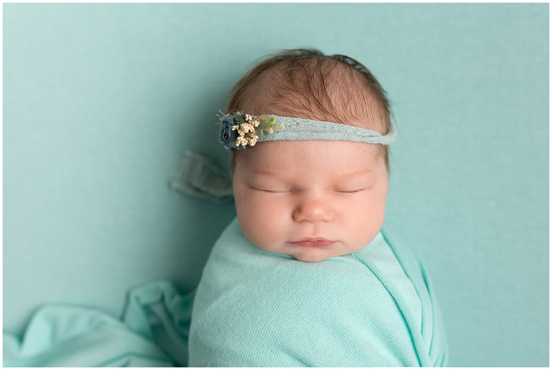 Close up of new baby girl wrapped by Lynne Harper in aqua with hair tie 