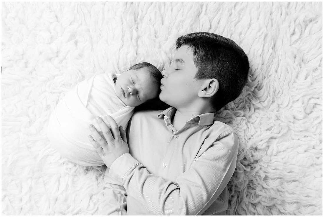 Adorable black and white image of brother kissing his new baby sister on her head by Lynne Harper Photography