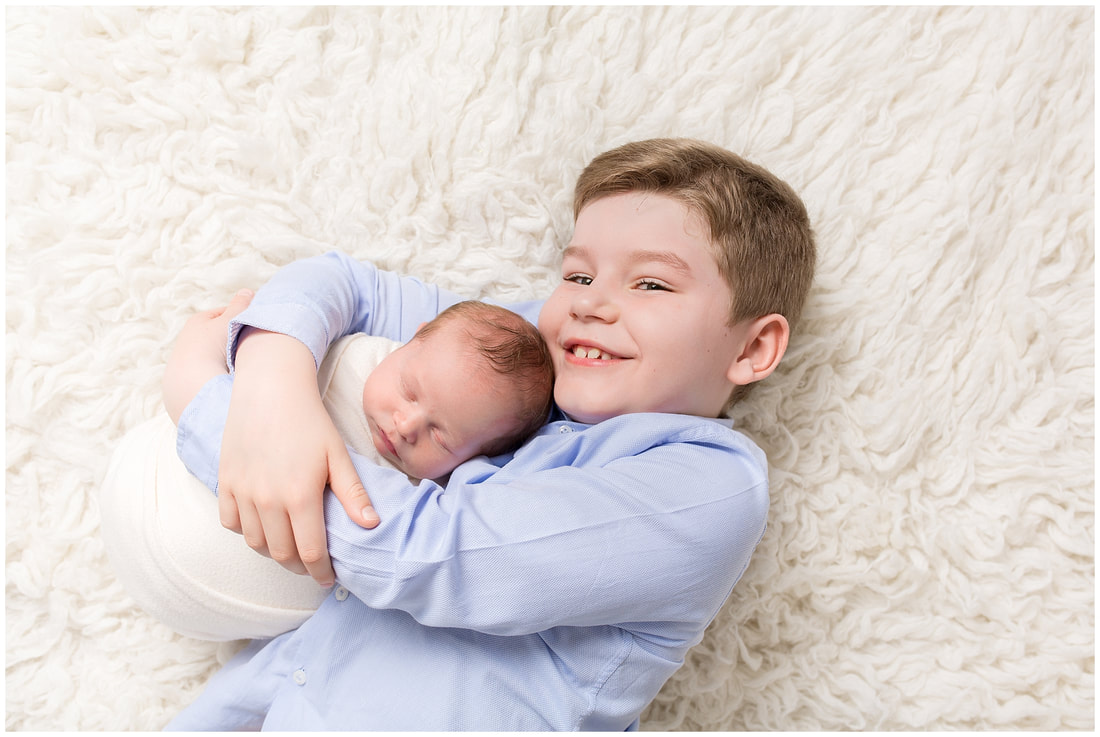 Image of proud big brother with baby sister by Lynne Harper Photography